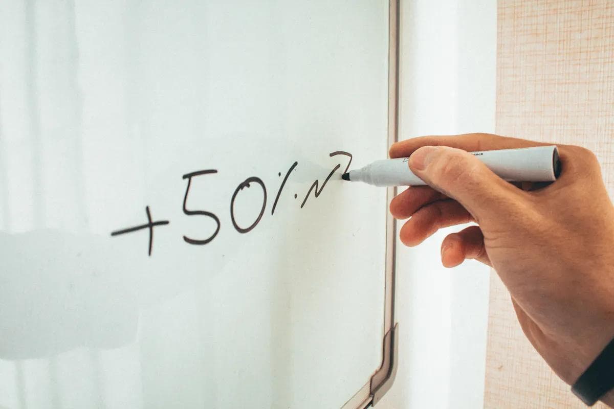 Hand writing '+50%' on a whiteboard, symbolizing business efficiency