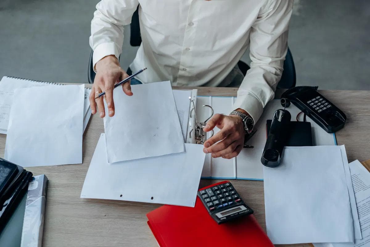 Person at desk with paperwork, phone, calculator, and ring binder.