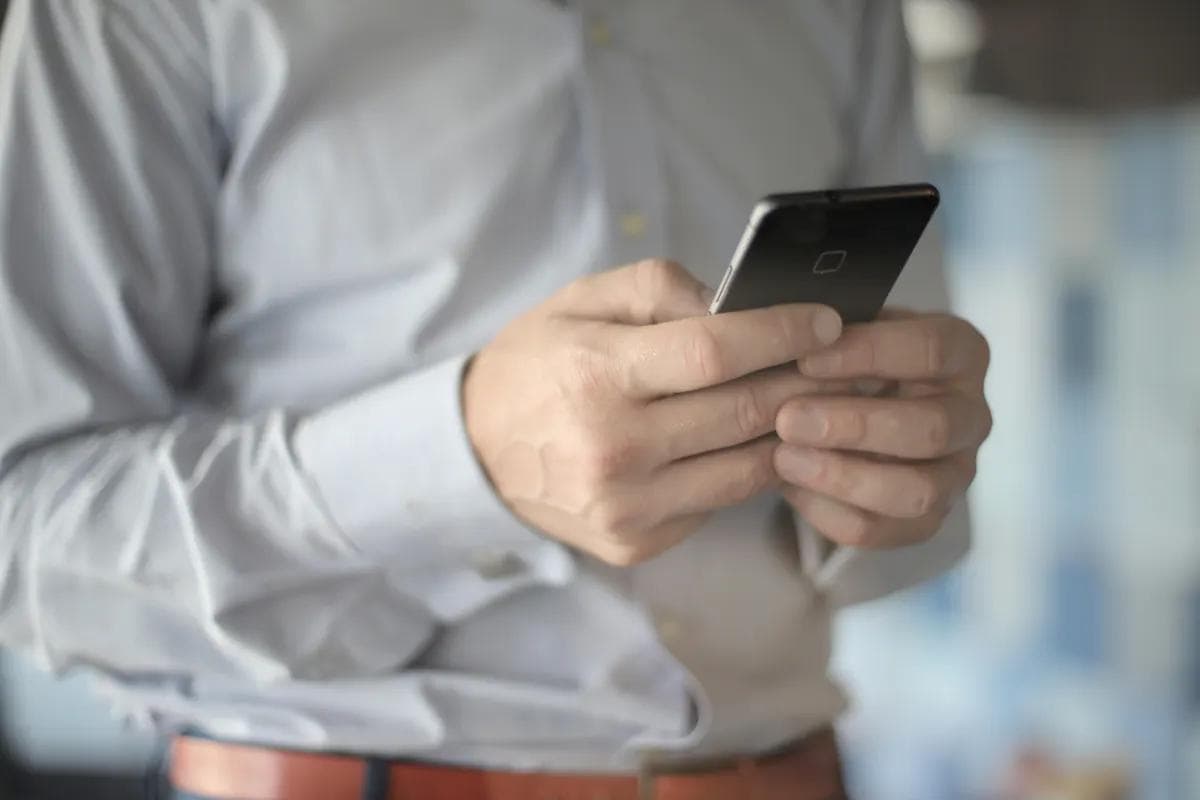 Man in dress shirt using smartphone for AI phone automation tasks.