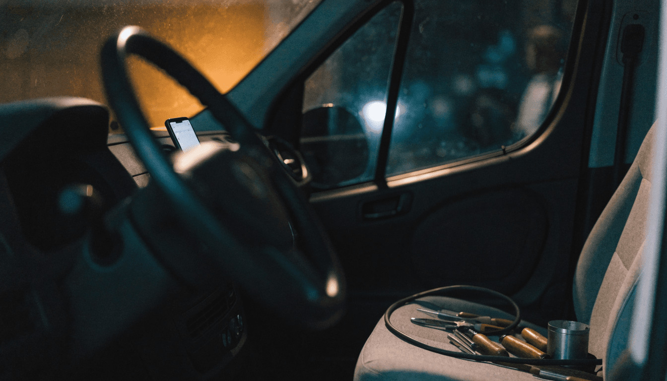 A phone glowing on the dashboard of an electrician's van parked after dark